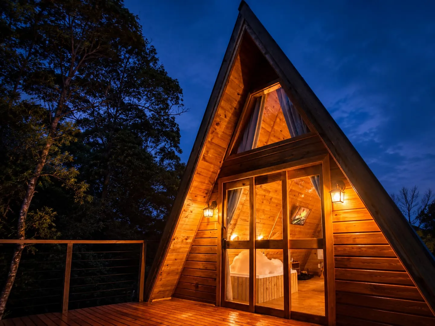 Chalé Âmbar, chalé em A de madeira iluminado à noite, com as portas abertas para o deck